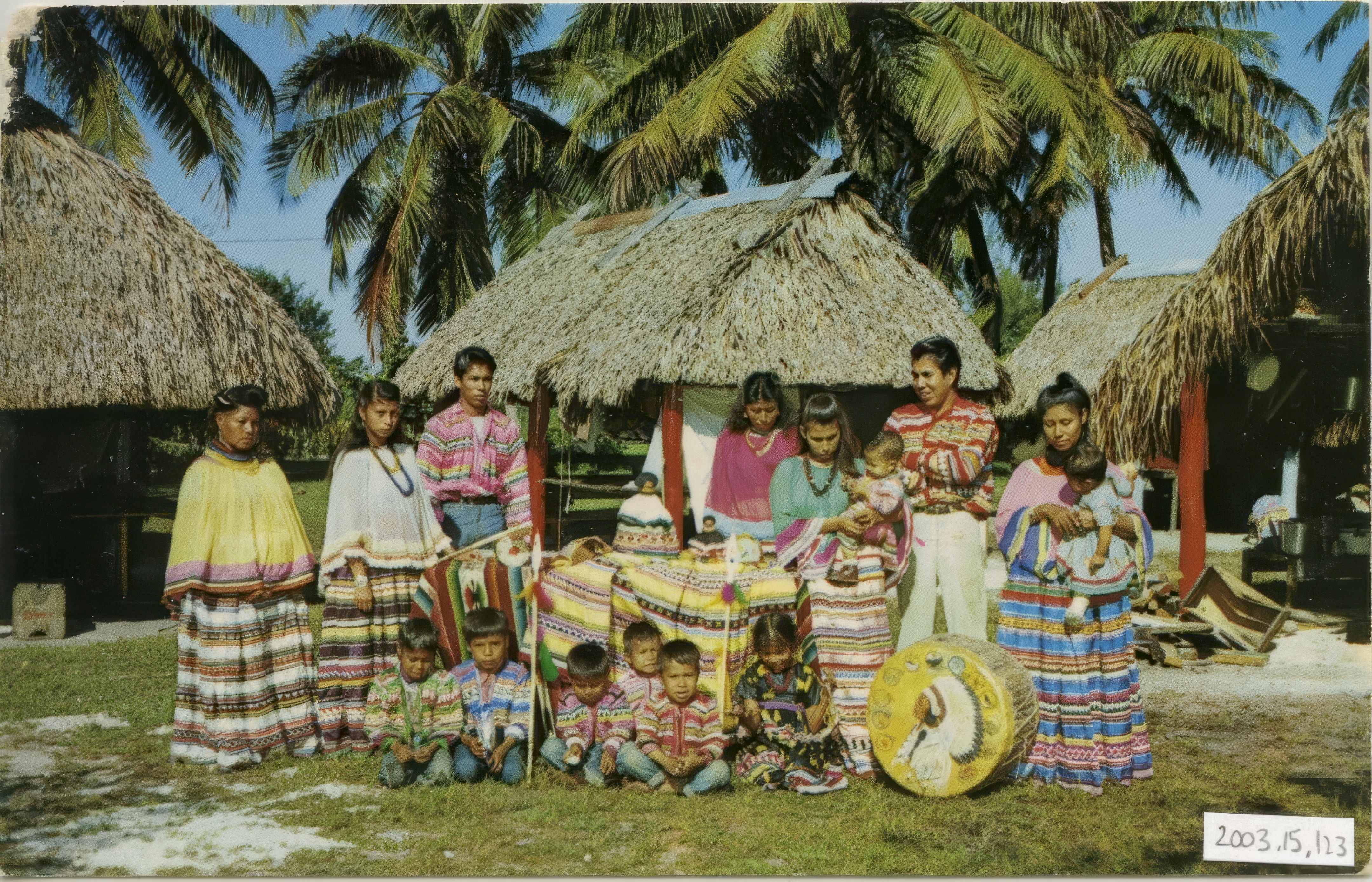 Historical photo of Miccosukee family in traditional patchwork clothing with chickee huts