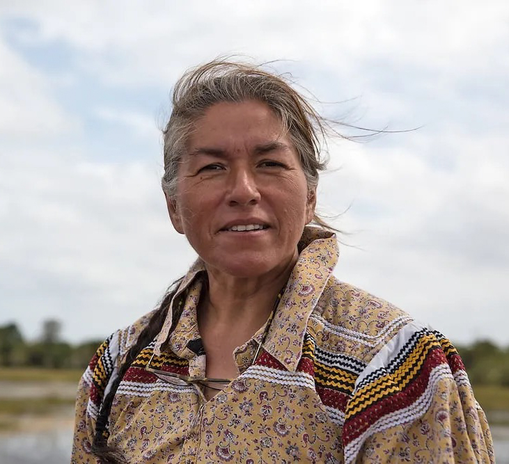 Betty Osceola smiling warmly in camouflage jacket with colorful scarf