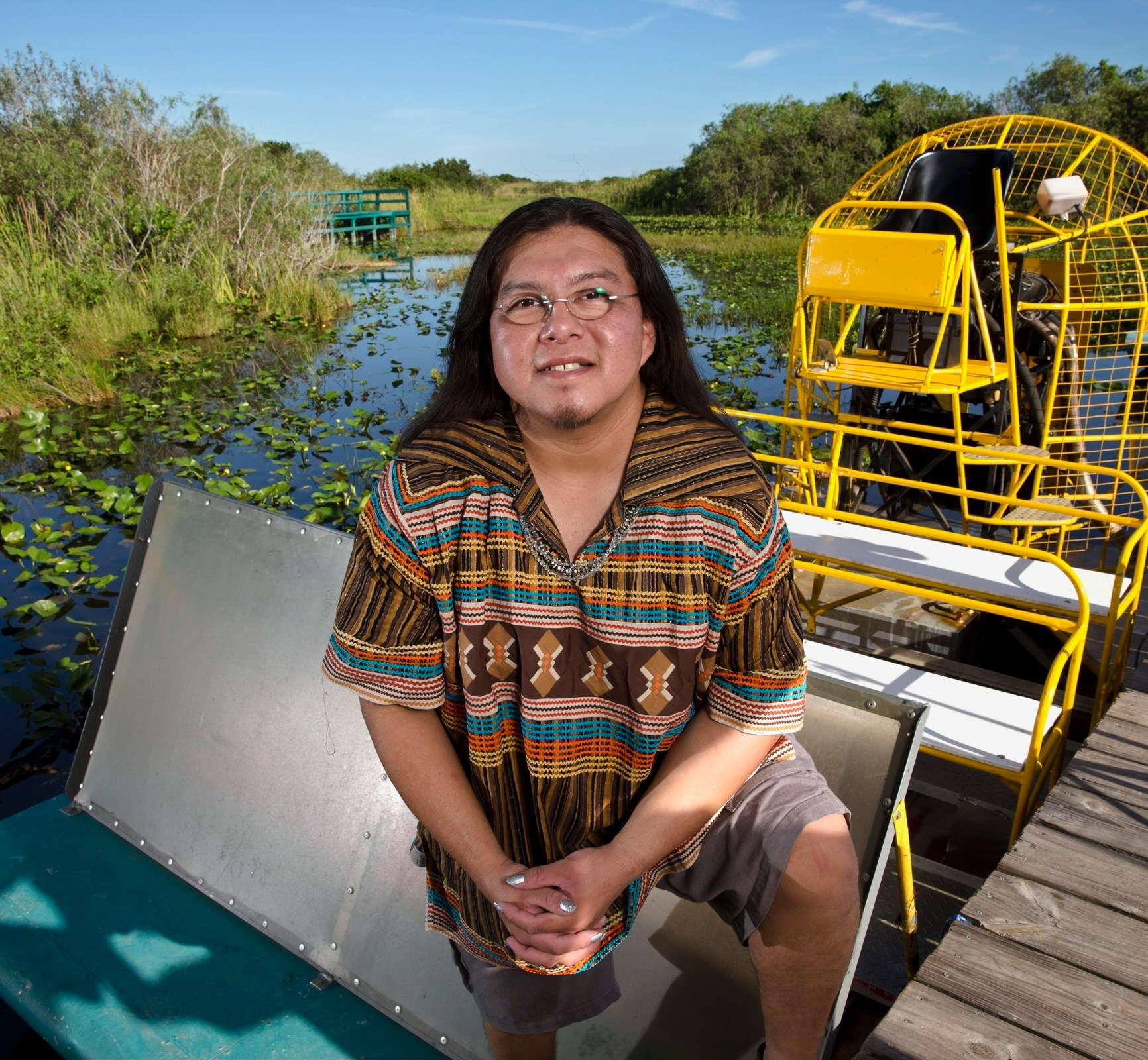 Houston Cypress wearing traditional Miccosukee patchwork shirt sitting on an airboat dock in the Everglades