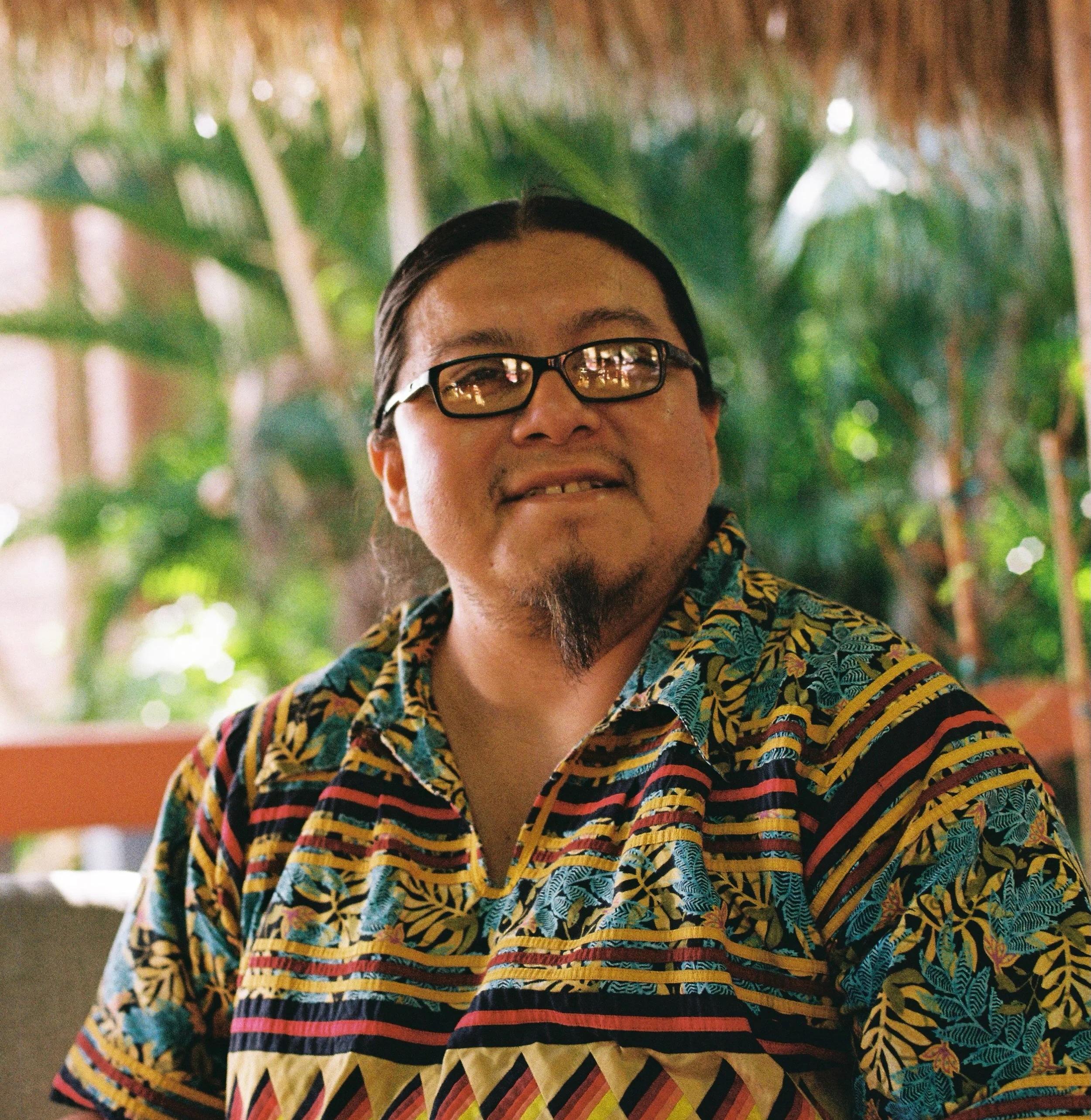 Houston Cypress wearing traditional Seminole patchwork shirt with tropical foliage behind him